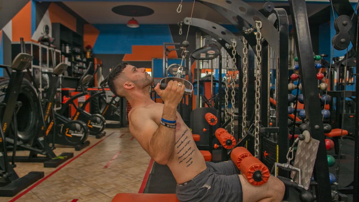 Tattooed man performs strength training on gym equipment, showcasing fitness.